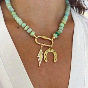 May include: A green opal beaded necklace with a gold clasp and three charms: a lightning bolt, a horseshoe, and a small green stone.