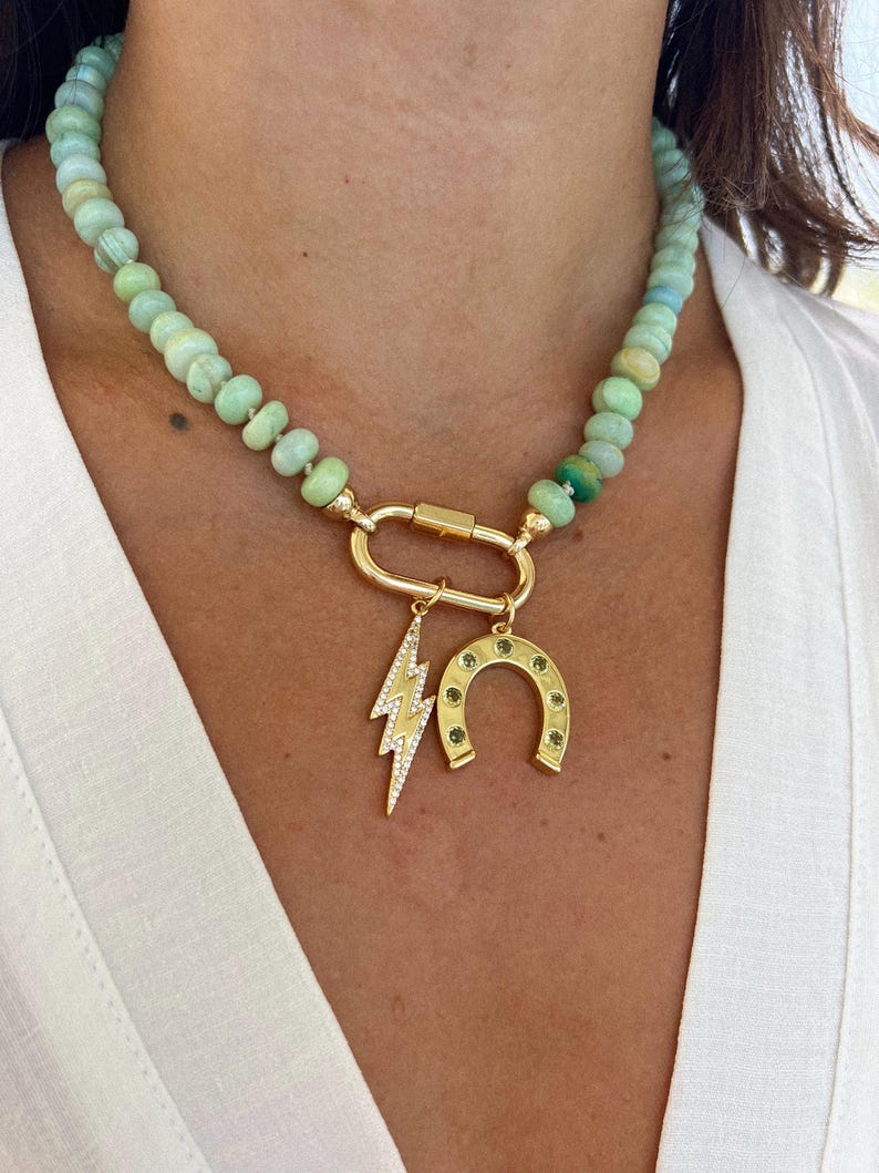 May include: A green opal beaded necklace with a gold clasp and three charms: a lightning bolt, a horseshoe, and a small green stone.