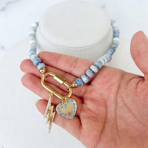 May include: A blue and white beaded necklace with a gold clasp and two charms: a lightning bolt and a heart with blue crystals.