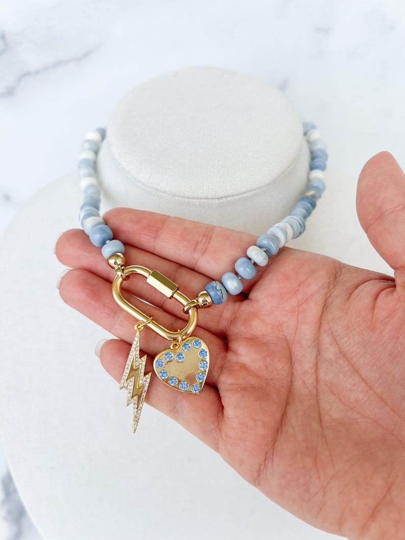 May include: A blue and white beaded necklace with a gold clasp and two charms: a lightning bolt and a heart with blue crystals.