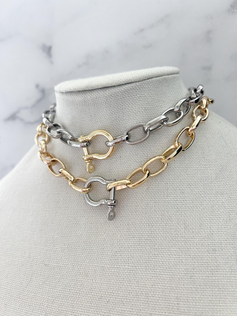 Puede incluir: Dos collares de cadena exhibidos en un maniqu&iacute;. Uno es dorado, el otro plateado. Ambos presentan eslabones ovalados grandes y un cierre de grillete. Probablemente sean bisuter&iacute;a.