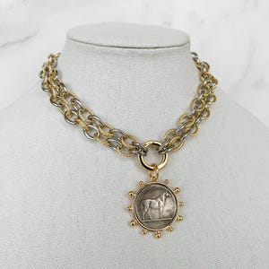 May include: A gold and silver chain necklace with a round pendant featuring a horse design.