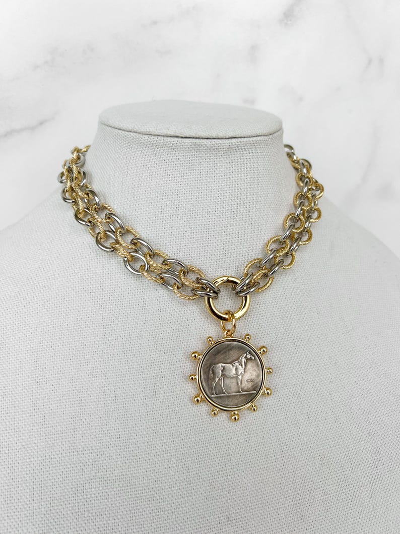 May include: A gold and silver chain necklace with a round pendant featuring a horse design.