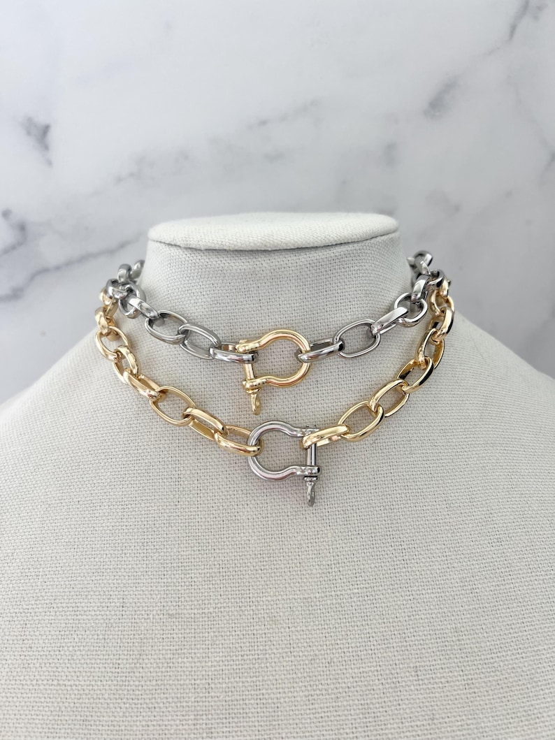 Puede incluir: Dos collares de cadena gruesa exhibidos en un maniqu&iacute;. Uno es dorado, el otro plateado. Ambos presentan eslabones ovalados grandes y un cierre decorativo. Los collares son probablemente bisuter&iacute;a.