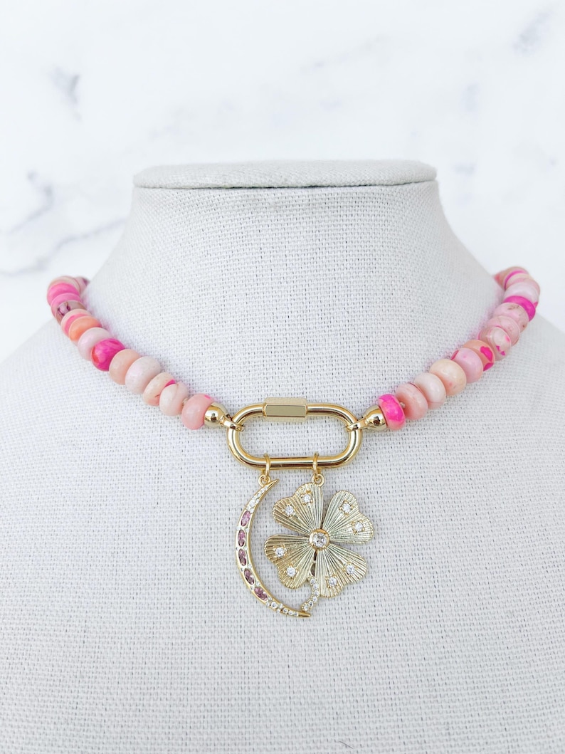 Pink Opal Hand Knotted Necklace featuring a large gold carabiner clasp in the front. Two charms are attached to the carabiner - a gold crescent moon charm with pink stones and a gold four leaf clover pendant with clear stone details