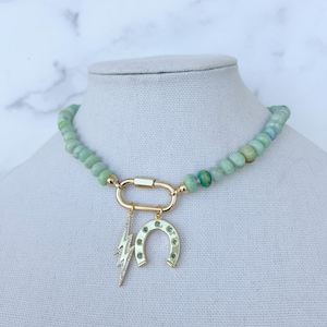 May include: A green jade beaded necklace with a gold clasp and two charms: a horseshoe and a lightning bolt. Both charms are adorned with small green stones.