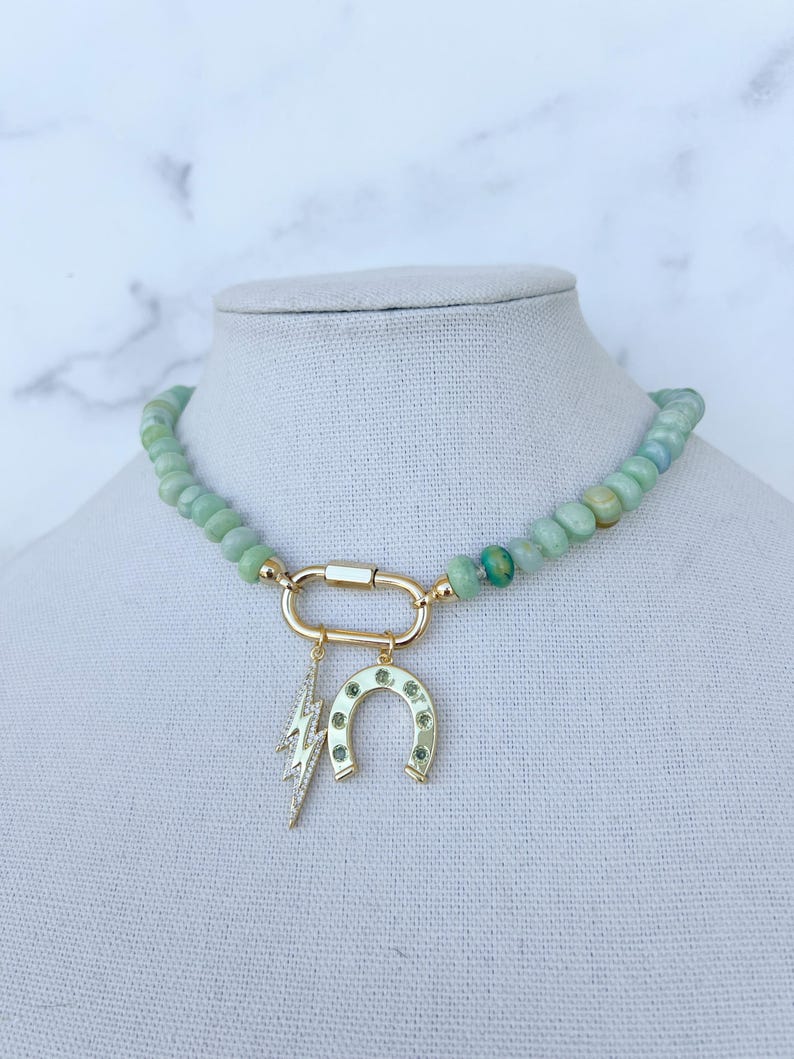 May include: A green jade beaded necklace with a gold clasp and two charms: a horseshoe and a lightning bolt. Both charms are adorned with small green stones.