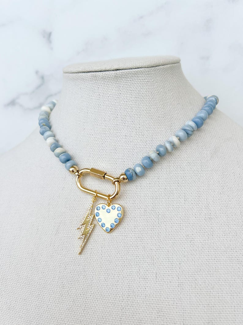 May include: A blue gemstone beaded necklace with a gold clasp and a charm featuring a heart with blue crystals and a lightning bolt.
