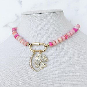 May include: A pink and white beaded necklace with a gold clasp and a charm featuring a crescent moon and a flower with rhinestones.