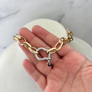 Puede incluir: Un collar de cadena dorada con un cierre plateado. El collar presenta eslabones grandes y ovalados y un cierre prominente en forma de U. La joya se exhibe sobre una cabeza de maniqu&iacute; blanca sobre un fondo de m&aacute;rmol.