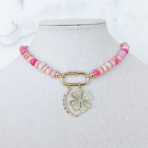 May include: A pink and white beaded necklace with a gold clasp and a charm featuring a crescent moon and a flower with rhinestones.