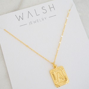 May include: Gold chain necklace with a gold pendant featuring the letter A. The pendant has a textured, ornate design. The necklace is displayed on a white card with the text "WALSH - JEWELRY" printed on it.