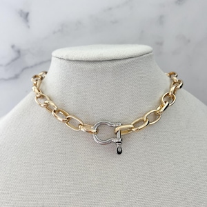 Puede incluir: Un collar de cadena dorada con un cierre plateado. El collar se exhibe en un maniqu&iacute;. Los eslabones de la cadena son ovalados y gruesos. El cierre tiene un dise&ntilde;o en forma de U con un peque&ntilde;o acento negro.