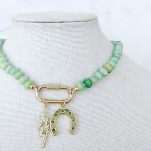 May include: A green jade beaded necklace with a gold clasp and two charms: a horseshoe and a lightning bolt. The charms are set with green gemstones.
