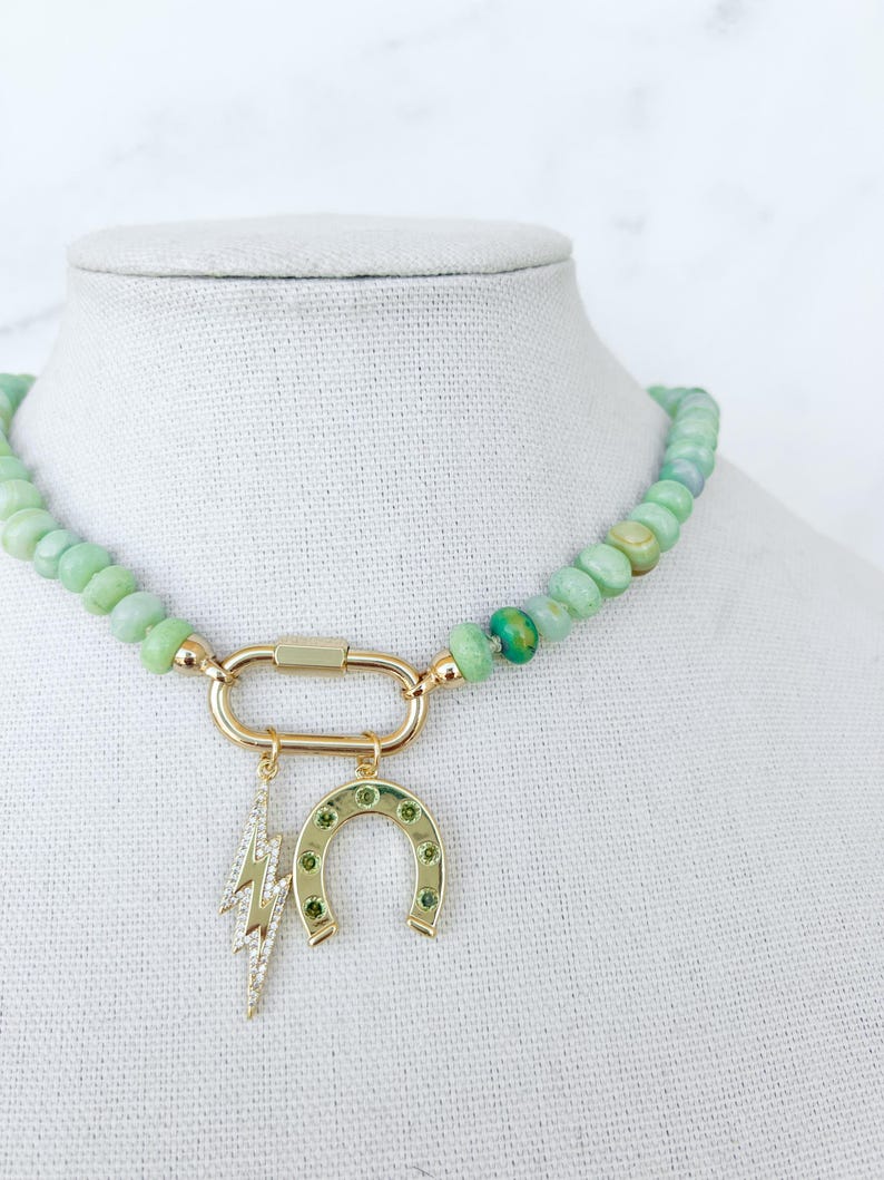 May include: A green jade beaded necklace with a gold clasp and two charms: a horseshoe and a lightning bolt. The charms are set with green gemstones.