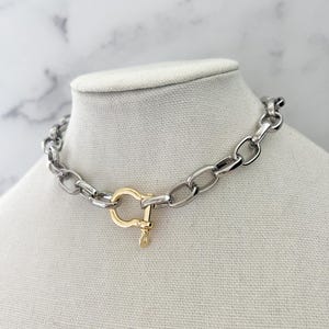 Puede incluir: Collar de cadena plateada con cierre dorado. El collar se exhibe sobre un busto de maniqu&iacute; blanco sobre un fondo de m&aacute;rmol. Los eslabones de la cadena son de forma ovalada.