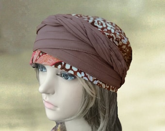 May include: A brown turban with a white and orange patterned fabric underneath. The turban is worn on a mannequin with blonde hair.