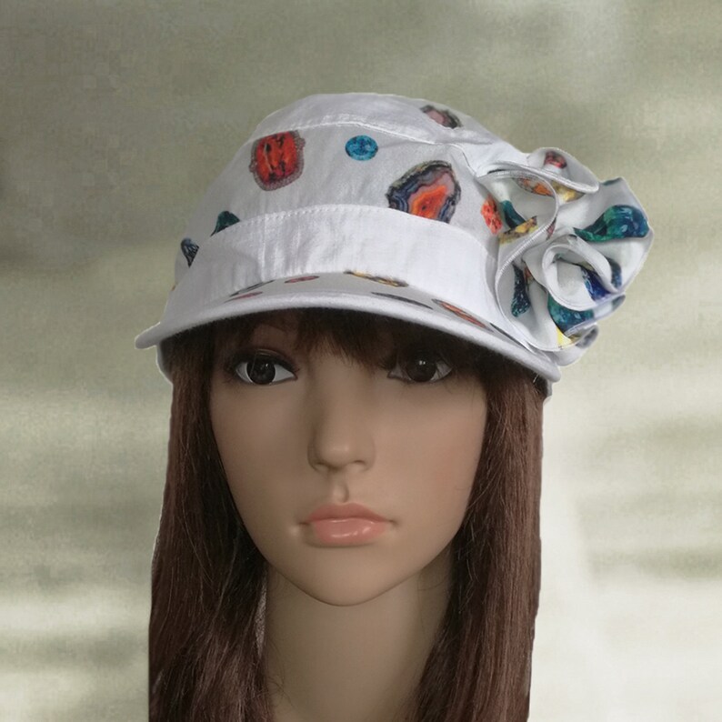 May include: A white cotton cap with a colorful patterned design and a large white flower on the side.