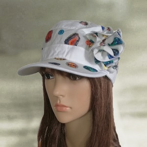 May include: White cotton cap with a colorful flower design. The cap has a short brim and a patterned design of colorful circles and swirls.