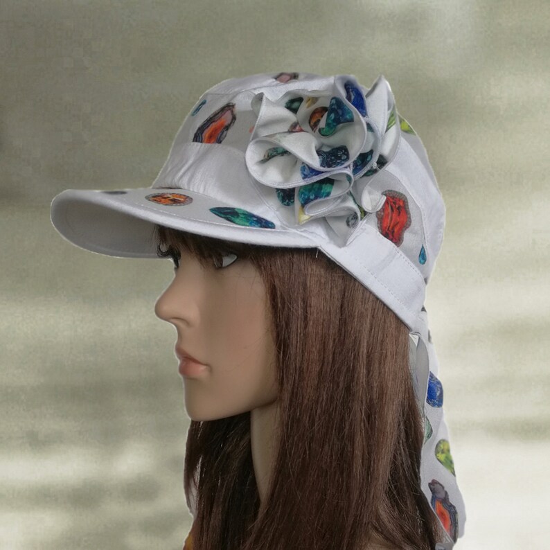 May include: White sun hat with a colorful flower design and a long tie. The hat has a wide brim and a small, round crown.