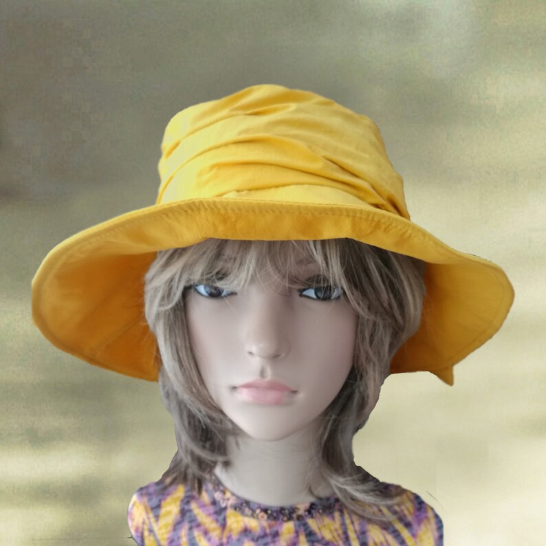 Puede incluir: Un sombrero de sol amarillo con un ala ancha y una corona fruncida. El sombrero est&aacute; hecho de una tela suave y ligera.