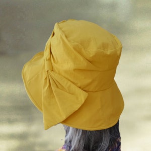 Puede incluir: Un sombrero de sol amarillo con un gran lazo en un lado. El sombrero est&aacute; hecho de una tela suave y ligera.