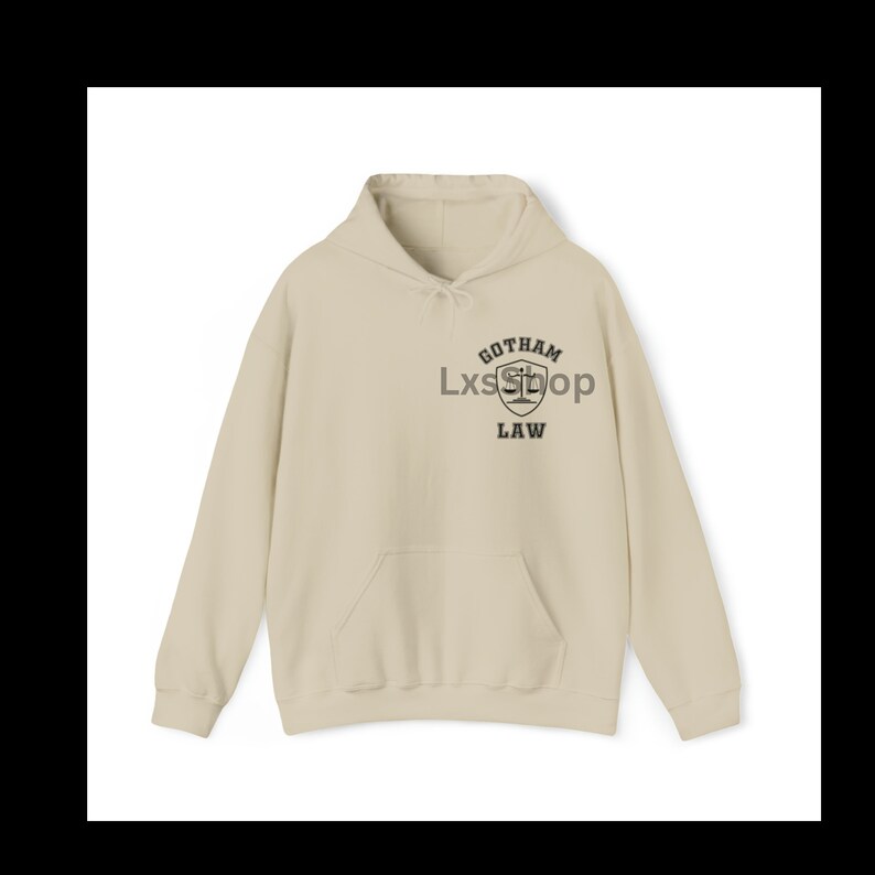 Op de afbeelding: Een beige hoodie met een zwarte grafische print van een schild met een weegschaal van de rechtvaardigheid en de tekst "Gotham Law".