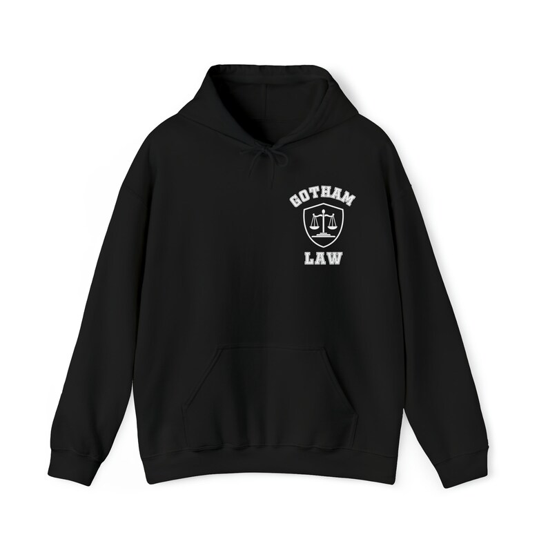 Op de afbeelding: Zwart hoodie met een witte afbeelding van een schild met een weegschaal van de rechtvaardigheid en de tekst "Gotham Law" erop.