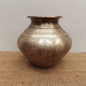 May include: A silver-colored, round metal pot with intricate etched designs. The pot has a wide body, a narrow neck, and a flared rim. The surface is covered in geometric and floral patterns. The pot is likely used for storage or decoration.