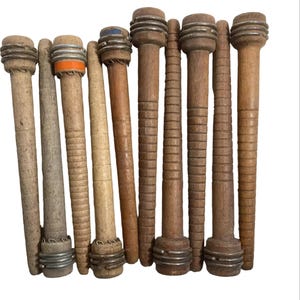 May include: A collection of ten vintage wooden textile bobbins arranged vertically. Each bobbin features a tapered cylindrical body with horizontal grooves, metal ferrules at the ends, and some include small colored bands in orange or blue.