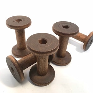 May include: A collection of five vintage wooden spools, each with a dark brown finish. The spools have a cylindrical body and a circular top and bottom. The spools are arranged on a white surface.