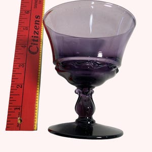 A purple glass wine glass with a flared bowl sits next to a red ruler on a white background.