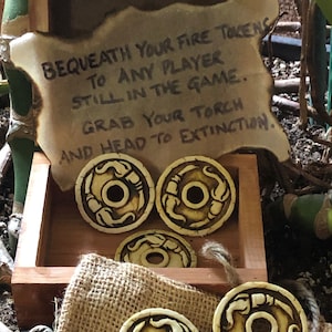 May include: Five brown and white fire tokens with a carved design of a dragon head. The tokens are in a wooden box with a burnt piece of paper that reads "BEQUEATH YOUR FIRE TOKENS TO ANY PLAYER STILL IN THE GAME. GRAB YOUR TORCH AND HEAD TO EXTINCTION."