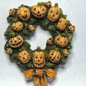 May include: A Halloween wreath with a orange bow, made of green leaves and orange pumpkins with carved faces.