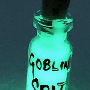 May include: A small glass bottle with a cork stopper filled with a glowing green liquid. The bottle is labeled "GOBLIN SPIT".
