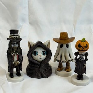 May include: Four Halloween figurines: a vampire, a cat in a cloak, a ghost cowboy, and a pumpkin-headed figure. The vampire wears a top hat and coat. The cat has blue eyes. The ghost wears a cowboy hat. The pumpkin figure wears a dress.