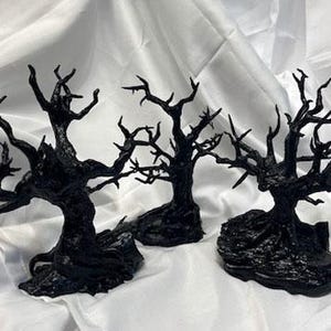 May include: Three black, skeletal tree sculptures with gnarled branches and twisted trunks. The trees are set on a black base and appear to be made of a resin material.