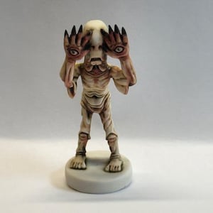 May include: A white figurine of a creature with long, thin fingers covering its eyes. The creature has a pale, fleshy body and a small, pointed head. The figurine is standing on a round base.