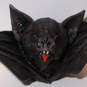 May include: A black bat figurine with outstretched wings and a red tongue. The bat has a detailed face with a sharp nose and teeth.