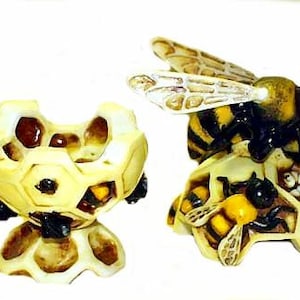 May include: A ceramic beehive with a bee on top. The beehive is open and has a honeycomb pattern. The bee is black and yellow with wings.