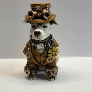 May include: A white ceramic figurine of a dog wearing a brown top hat with goggles, a brown jacket with gold accents, and a yellow flower. The dog is wearing a silver collar with a peace sign charm.