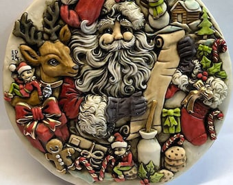 Może przedstawiać: Ceramiczny talerz świąteczny przedstawiający szczegółowy wizerunek Świętego Mikołaja trzymającego zwoje, otoczonego świątecznymi elementami, takimi jak renifer, elfy, prezenty, laski cukrowe i ciasteczka.