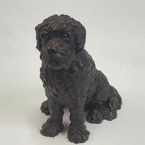 May include: A black, ceramic figurine of a dog sitting with its paws crossed. The dog has a curly coat and a serious expression.