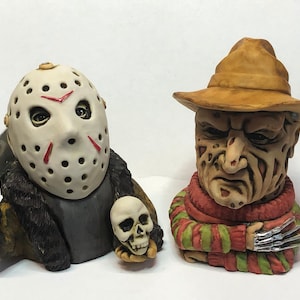 Può includere: Due figurine in ceramica di cattivi di film horror. La prima è Jason Voorhees di Venerdì 13, con la sua iconica maschera da hockey e che tiene un coltello e un teschio. La seconda è Freddy Krueger di Nightmare on Elm Street, con il suo caratteristico maglione a righe e un fedora marrone.