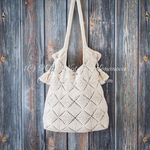 May include: A beige crocheted tote bag with a diamond pattern hangs against a weathered wood background. The bag has two tassels on each side.