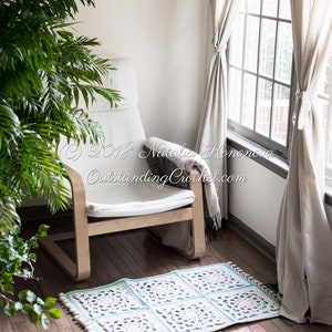Puede incluir: Una silla blanca con una alfombra de crochet delante. La alfombra est&aacute; hecha de hilo blanco y azul claro y tiene un dise&ntilde;o floral. La silla est&aacute; en una habitaci&oacute;n con paredes blancas y una ventana con cortinas blancas.