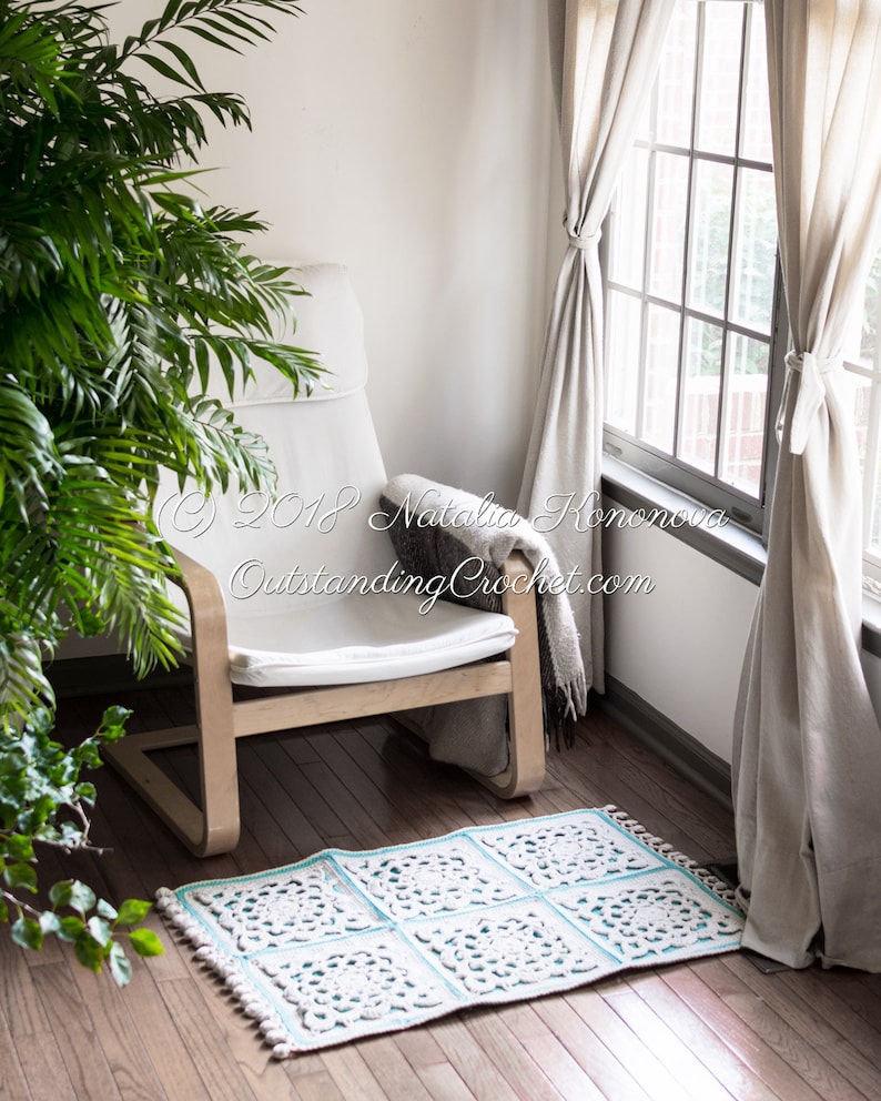 Puede incluir: Una silla blanca con una alfombra de crochet delante. La alfombra est&aacute; hecha de hilo blanco y azul claro y tiene un dise&ntilde;o floral. La silla est&aacute; en una habitaci&oacute;n con paredes blancas y una ventana con cortinas blancas.
