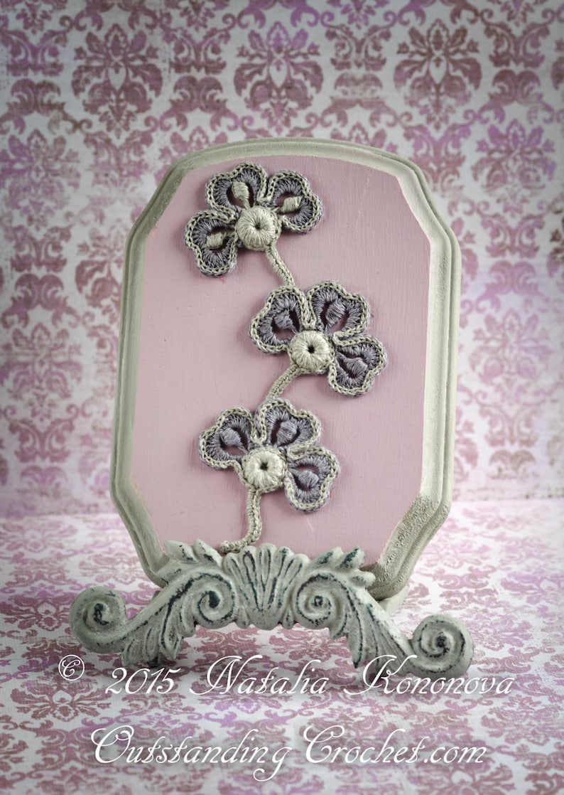 May include: A pink wooden plaque with a grey crocheted flower design. The plaque is on a white stand with a decorative scroll design. &copy; 2015 Natalia Kononova Outstanding Crochet.com