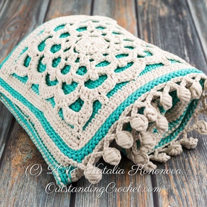 Puede incluir: Un coj&iacute;n de punto de crochet con un dise&ntilde;o de mandala blanco y turquesa. El coj&iacute;n tiene un borde de flecos con borlas.