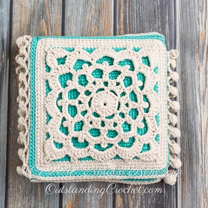 Puede incluir: Una almohada cuadrada de crochet con un dise&ntilde;o de crochet blanco sobre un fondo turquesa. La almohada tiene un borde de flecos y est&aacute; fotografiada sobre una superficie de madera.